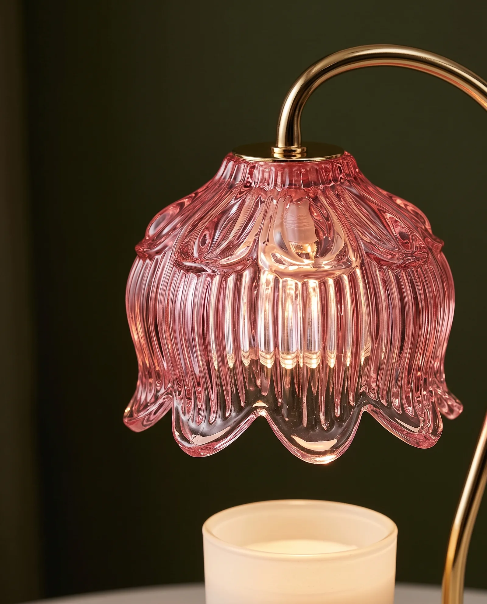 Close-up of the lamp's pink ribbed glass shade with scalloped edge, lit from inside, above a white candle